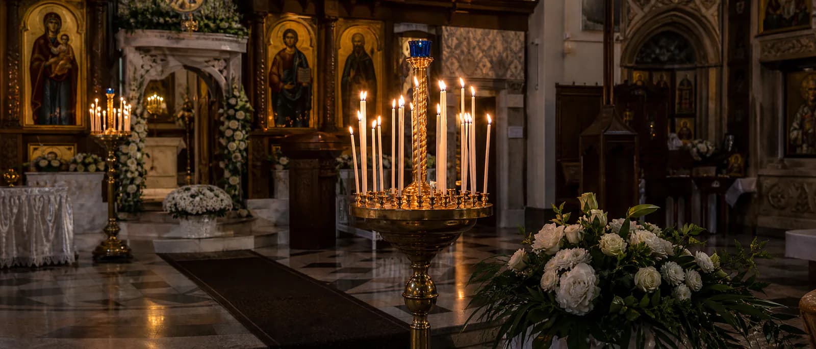 Interior de biserică ortodoxă cu lumânări aprinse și flori albe pentru slujba funerară