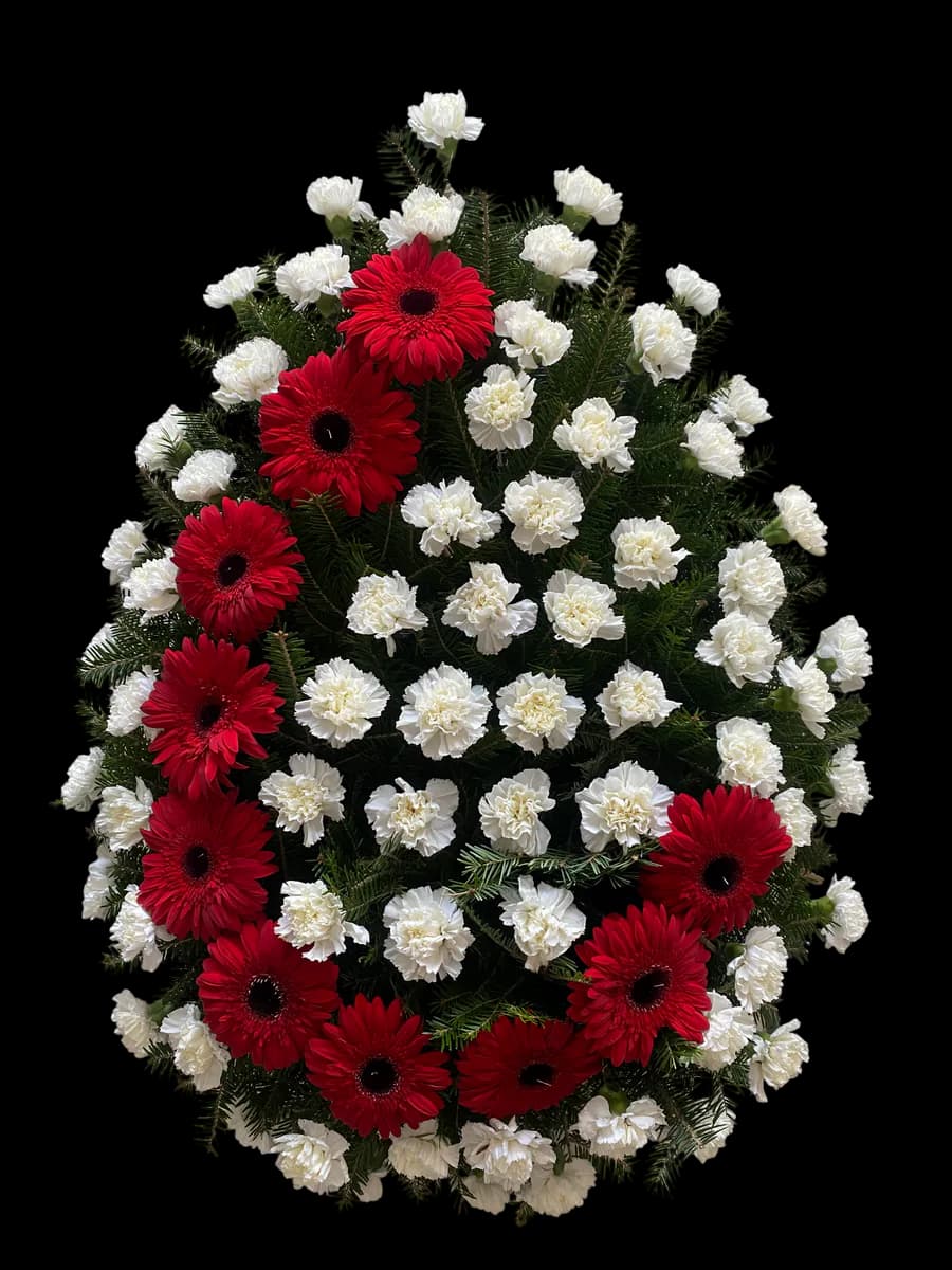 Coroană funerară cu gerbere roșii și garoafe albe pe fond de brad